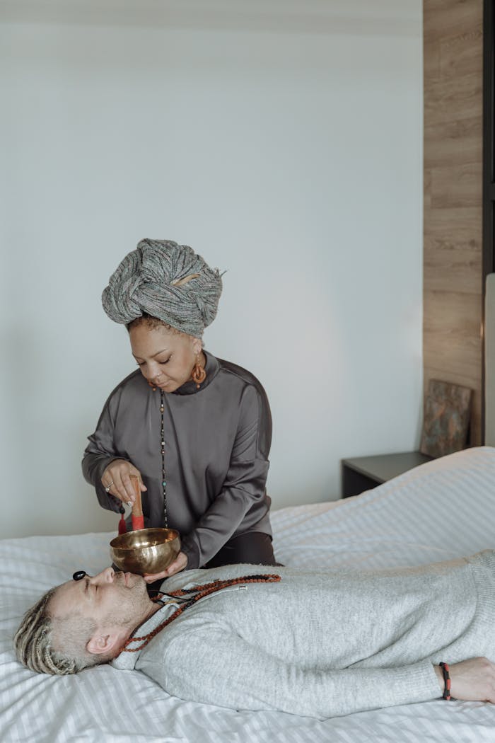 A woman performs a sound therapy session using a singing bowl on a resting person.