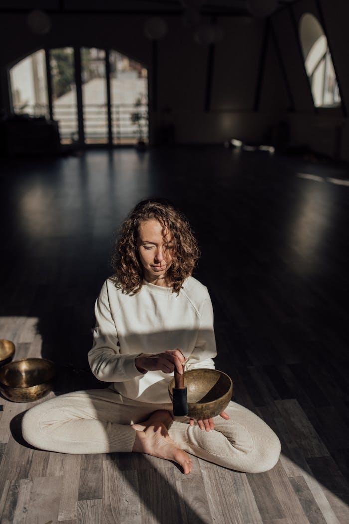 Woman meditating with a Tibetan singing bowl in a serene indoor setting, bathed in natural light for peaceful ambience.