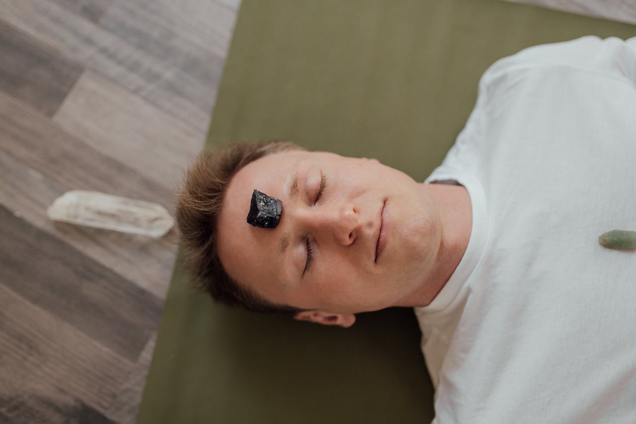 A man lying down with a healing crystal on his forehead for relaxation and wellbeing.