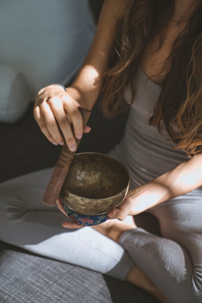 A woman meditates while holding and playing a Tibetan singing bowl indoors.